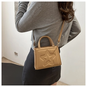 Detail of light brown crossbody bag with star embossed design shown on model shoulder