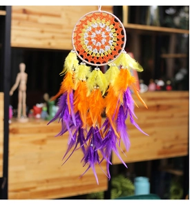 Close-up of colorful handmade dreamcatcher with yellow and orange feathers on wood shelf
