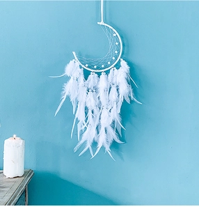 Detailed view of a crescent moon dreamcatcher with white feathers and beads on blue wall
