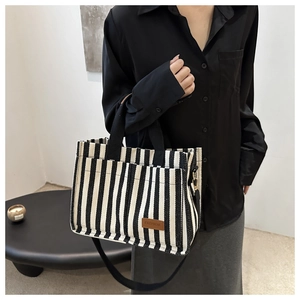 Detail of striped canvas tote bag with front pocket and removable strap shown on model