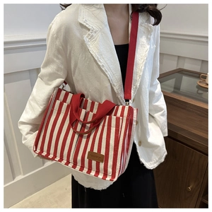 Lifestyle view of striped canvas tote bag with red handles and adjustable shoulder strap