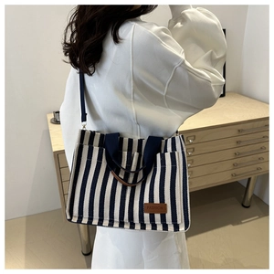 Detail of blue and white striped canvas tote with brown leather patch and woven handles