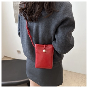Detail view of red mini crossbody phone bag with pearl buckle and braided strap on model