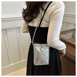 Detail of silver metallic mini bag featuring a pearl clasp and twisted woven shoulder strap