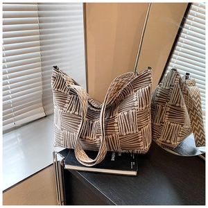 Detail of a brown and beige jacquard tote bag with geometric wide strap on a wooden desk