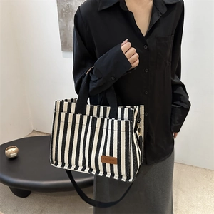 Minimalist black and white striped canvas tote bag with brown leather patch and woven handles