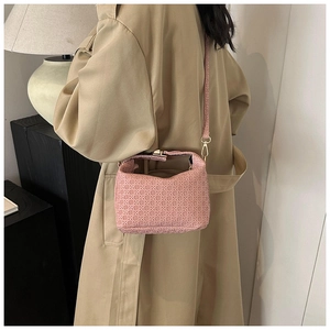 Detail of pink woven leather crossbody bag with gold hardware worn over a beige coat