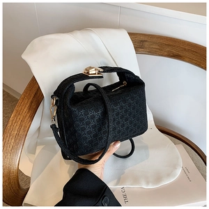 Detail of black woven pillow bag with gold clasp shown on a wooden chair with a white blazer