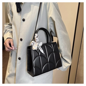 Detalle de bolso bandolera negro acolchado con diseño festoneado y asa con pañuelo