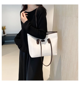 Detail view of large white tote bag with brown leather straps worn by model on shoulder