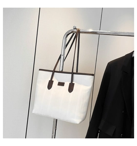 Detailed view of large white tote bag with vertical stripes and brown leather logo tag