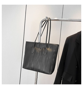 Detail of black tote bag featuring vertical embossed texture and central metal logo plate