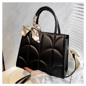 Detalle de bolso negro estructurado con costuras festoneadas y pañuelo de seda decorativo