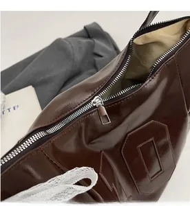Detailed close-up of smooth silver metal zipper and dark brown leather texture of the bag