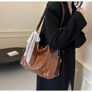Close-up of brown glossy tote bag with decorative stitching and a white lace bow pendant