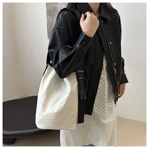 Détail d'un sac seau en toile blanche avec bandoulière en cuir noir porté par un modèle