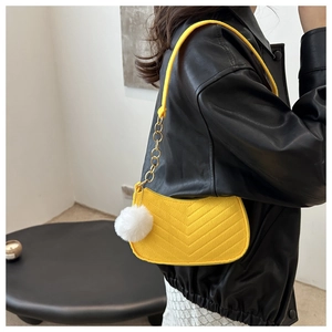 Detail of yellow quilted crossbody bag with gold chain strap and fluffy white pompom charm