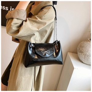 Détail du sac à bandoulière noir brillant avec nœud argenté et chaîne sur un manteau