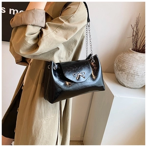 Détail d'un sac à bandoulière en cuir verni noir avec boucle noeud doré