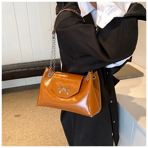 Détail du sac croissant marron brillant avec nœud argenté et bandoulière chaîne