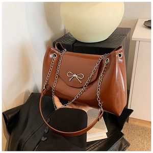 Détail d'un sac cabas marron brillant avec nœud en argent et bandoulière en chaîne