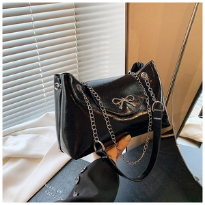 Détail du sac bandoulière en cuir verni noir avec nœud métallique argenté et chaîne
