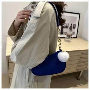 Detail of dark blue V-quilted underarm bag with gold chain and white pompom charm
