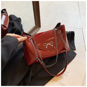 Détail d'un sac cabas en cuir verni bordeaux avec nœud argenté et bandoulière