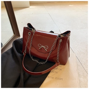 Détail du sac à bandoulière en cuir verni bordeaux avec nœud argenté et chaîne