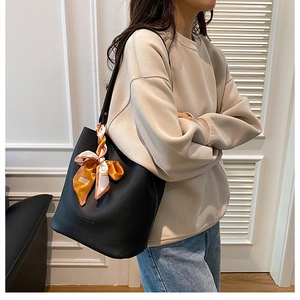 Détail du sac seau noir en cuir grainé avec une poignée ornée d'un foulard en soie