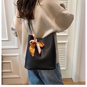 Détail du sac seau noir en cuir grainé avec foulard décoratif en soie imprimé et rivets dorés