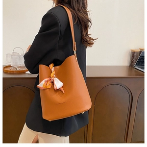 Sac seau en cuir marron avec détail foulard en soie porté par un mannequin en intérieur