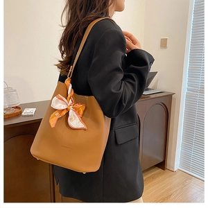 Sac seau marron en cuir grainé avec foulard en soie à motifs porté par un mannequin