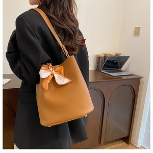 Détail du sac seau en cuir caramel avec foulard décoratif et clous de protection dorés
