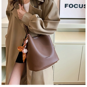 Détail du sac seau en cuir marron foncé avec texture grainée et accessoire foulard en soie
