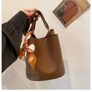 Détail du sac seau en cuir marron foncé avec motif litchi et foulard en soie
