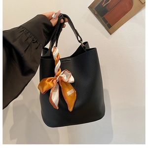 Détail d'un sac seau en cuir grainé noir avec un foulard décoratif en soie imprimée