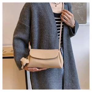Detail of beige litchi grain leather crossbody bag with a cute elephant charm