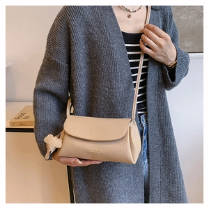 Beige crossbody bag with elephant charm worn with a stylish long grey cardigan