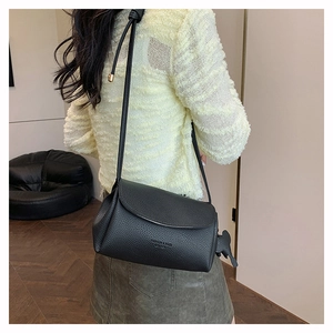 Close-up of black lychee grain cylinder bag with dinosaur charm on a female model