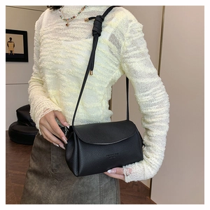 Detail of a black crossbody bag with lychee texture and knot shoulder strap detail