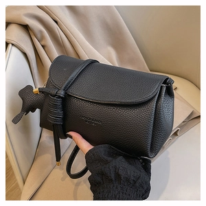 Detail of black pebble grain leather crossbody bag with a dog charm and knotted strap