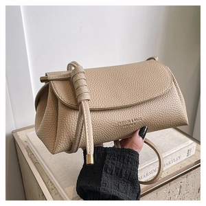 Close-up of beige pebbled leather handbag featuring a knotted strap on an art book