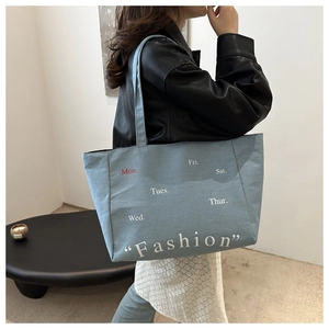 Detail of light blue denim tote bag with Monday print shown on a model in black leather jacket