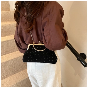 Detail of black velvet polka dot shell bag with gold chain strap on a model