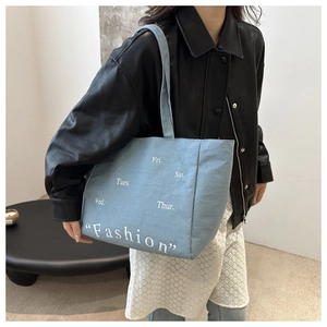 Detail of light blue denim tote bag with white Fashion print and shoulder strap