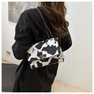 Detail of a cow print crossbody bag with metal chain strap and flap lock closure