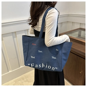 Detail of blue denim tote bag featuring white day-of-week typography and fashion print