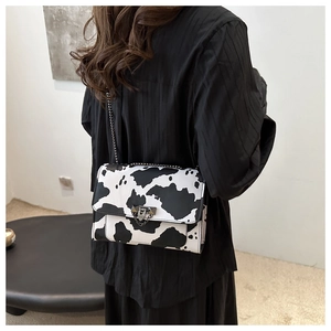 Detail view of the chic cow print crossbody bag with metal chain strap on model