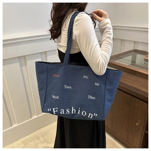 Detail of dark blue denim tote bag featuring white Fashion text and daily embroidery